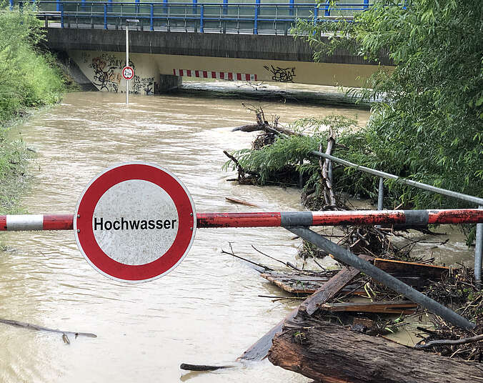 Rotach mit braunem schnell fließendem Wasser und einem Hinweisschild Hochwasser