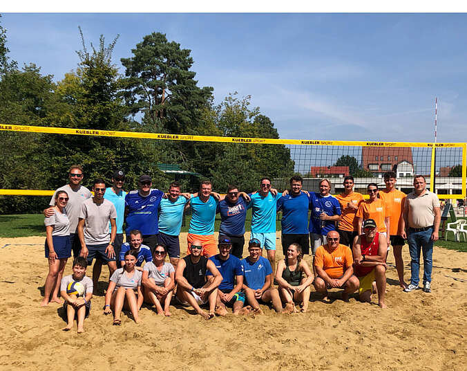 Männer und Frauen stehen im Sand vor einem Volleyballnetz