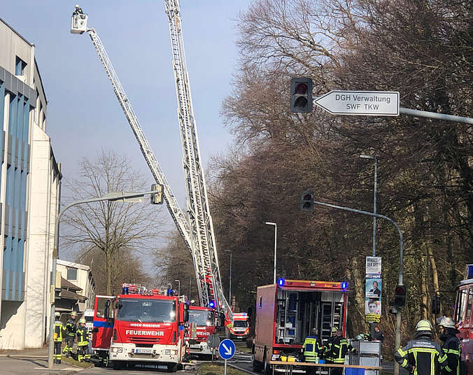 Feuerwehrfahrzeuge, eine ausgefahrene Drehleiter und viele Einsatzkräfte in Feuerwehrkleidung auf der Straße vor einem großen Gebäude