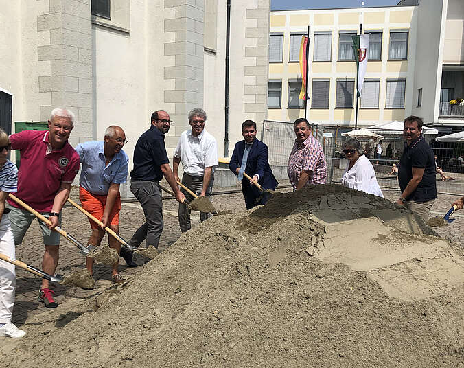 Spatenstich: Männer und Frauen mit Spaten hinter einem Berg Sand